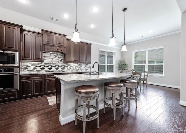 kitchen with appliances with stainless steel finishes, a center island with sink, hanging light fixtures, and sink