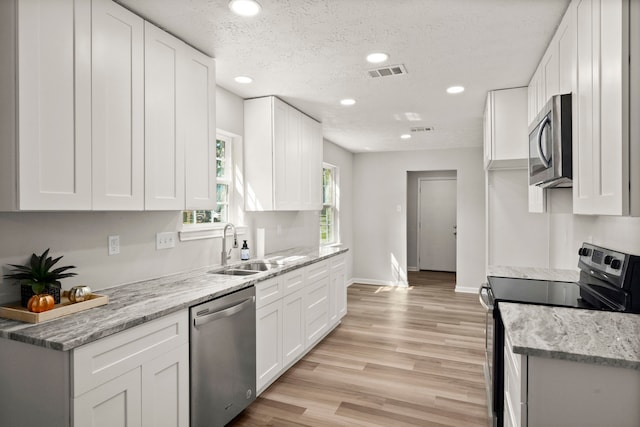 kitchen featuring light wood-type flooring, a textured ceiling, stainless steel appliances, sink, and white cabinetry