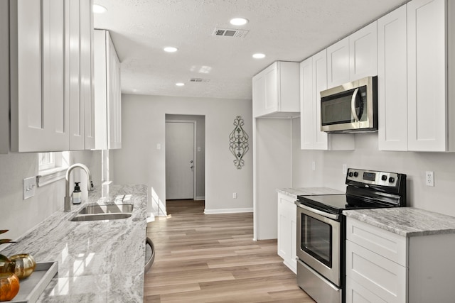 kitchen with appliances with stainless steel finishes, light stone counters, white cabinetry, and sink