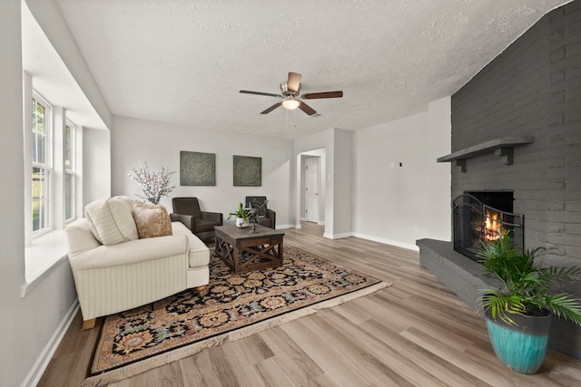 living room with a textured ceiling, hardwood / wood-style flooring, a brick fireplace, and ceiling fan