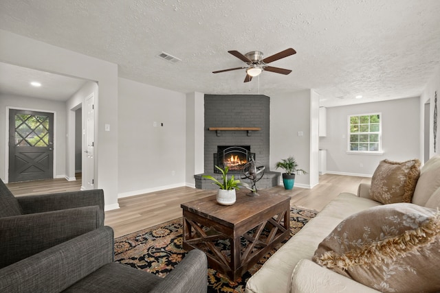 living room featuring a fireplace, ceiling fan, a textured ceiling, and light hardwood / wood-style flooring