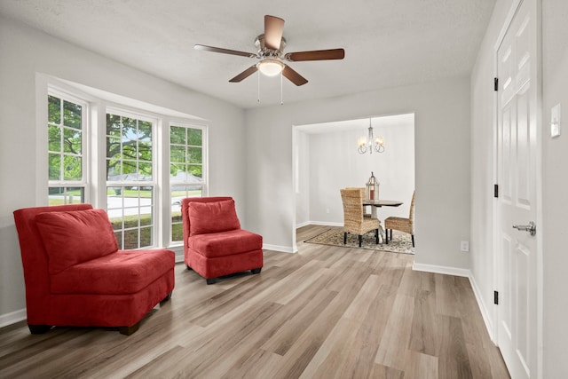 sitting room with ceiling fan with notable chandelier, light hardwood / wood-style floors, and a textured ceiling