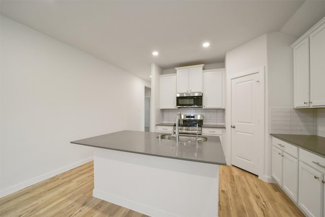 kitchen featuring sink, appliances with stainless steel finishes, a kitchen island with sink, white cabinetry, and light wood-type flooring