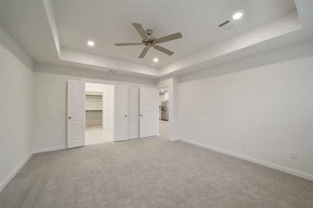 unfurnished bedroom featuring a walk in closet, ceiling fan, stainless steel fridge with ice dispenser, a raised ceiling, and light carpet