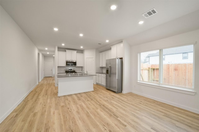 kitchen with light hardwood / wood-style flooring, appliances with stainless steel finishes, an island with sink, decorative backsplash, and white cabinets