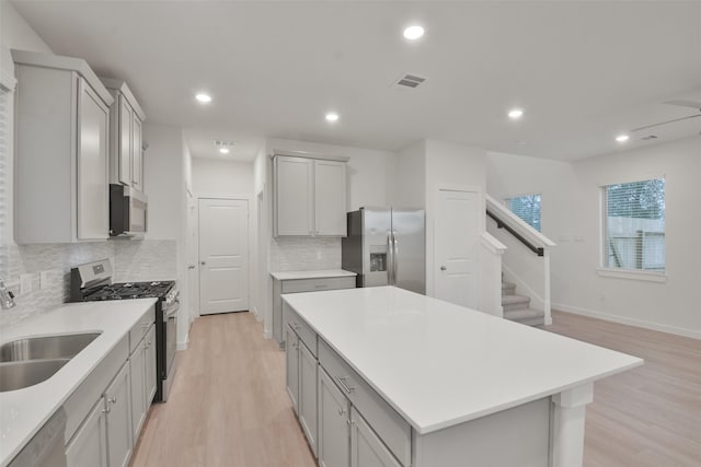 kitchen featuring gray cabinetry, a center island, sink, decorative backsplash, and stainless steel appliances