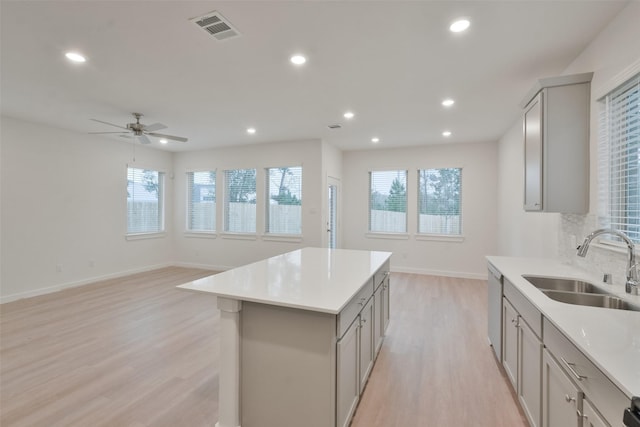 kitchen with sink, light hardwood / wood-style flooring, stainless steel dishwasher, gray cabinets, and a kitchen island