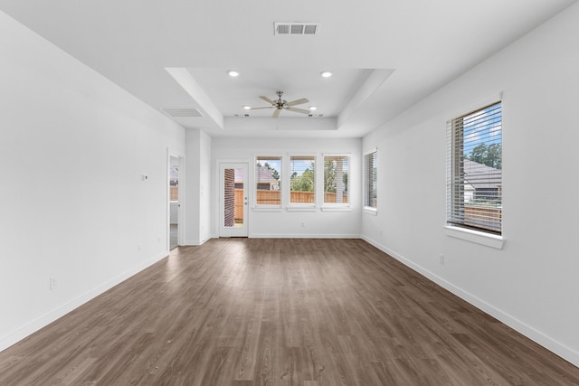 unfurnished living room featuring a tray ceiling, ceiling fan, and dark wood-type flooring