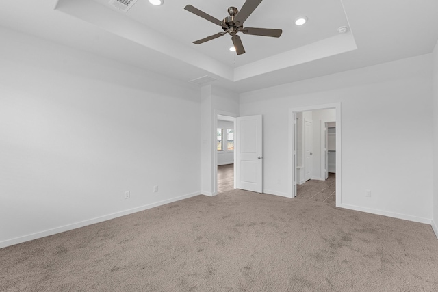 unfurnished bedroom with a raised ceiling, a walk in closet, ceiling fan, and light carpet