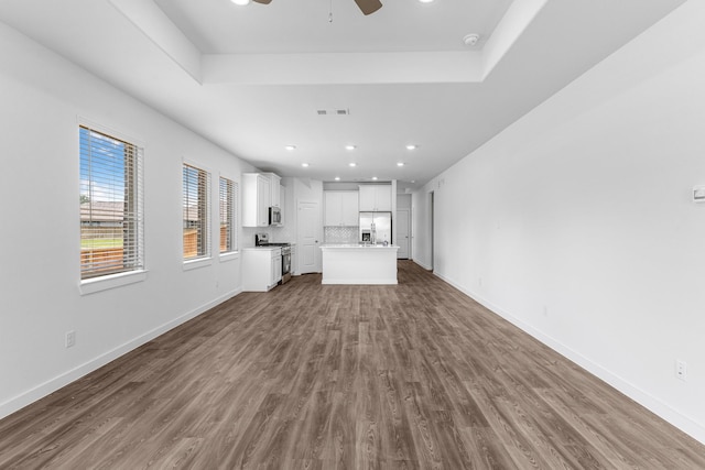 unfurnished living room with dark hardwood / wood-style floors, ceiling fan, and a tray ceiling