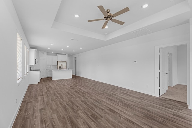 unfurnished living room with a raised ceiling, ceiling fan, and hardwood / wood-style floors