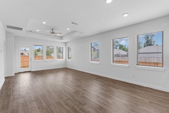 empty room featuring a raised ceiling, ceiling fan, and dark wood-type flooring