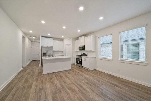 kitchen featuring appliances with stainless steel finishes, an island with sink, sink, white cabinets, and light wood-type flooring