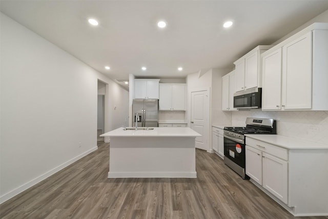 kitchen with dark wood-type flooring, white cabinetry, a center island with sink, stainless steel appliances, and decorative backsplash