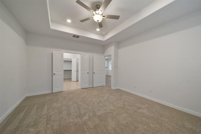 unfurnished bedroom with a raised ceiling, a spacious closet, light carpet, and ceiling fan