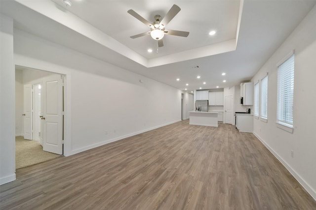 unfurnished living room with light hardwood / wood-style floors, a raised ceiling, and ceiling fan