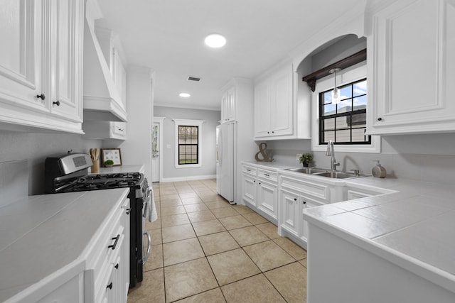 kitchen featuring white cabinetry, stainless steel gas stove, white refrigerator, tile countertops, and light tile patterned floors