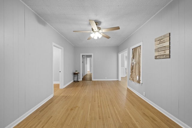 empty room with ceiling fan, wood walls, light wood-type flooring, and a textured ceiling