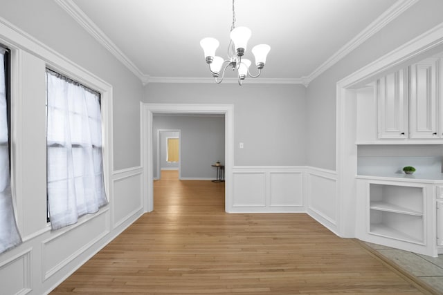 unfurnished dining area featuring plenty of natural light, light hardwood / wood-style floors, ornamental molding, and an inviting chandelier