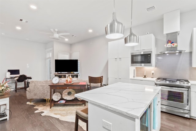 kitchen featuring pendant lighting, white cabinets, built in microwave, tasteful backsplash, and stainless steel range oven