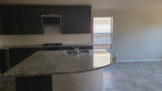 kitchen featuring decorative backsplash, black gas stovetop, sink, dark stone countertops, and an island with sink