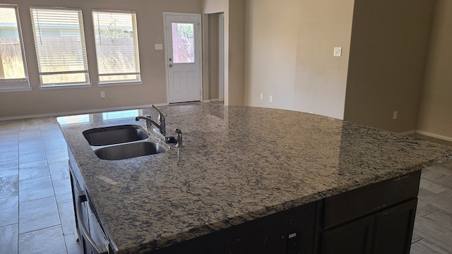 kitchen featuring light stone countertops, an island with sink, and sink