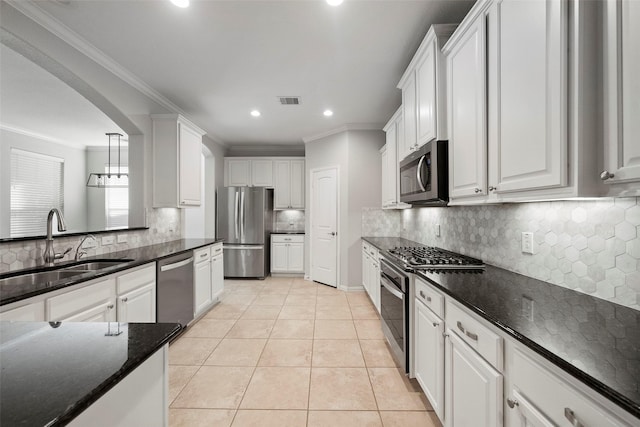 kitchen featuring white cabinetry, stainless steel appliances, dark stone counters, light tile patterned flooring, and ornamental molding