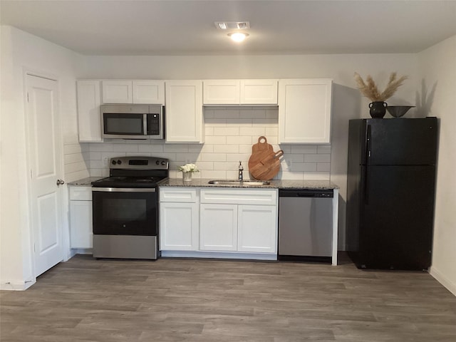 kitchen with appliances with stainless steel finishes, dark stone counters, sink, wood-type flooring, and white cabinets