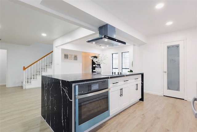 kitchen with wall chimney range hood, oven, a center island, light hardwood / wood-style floors, and white cabinetry