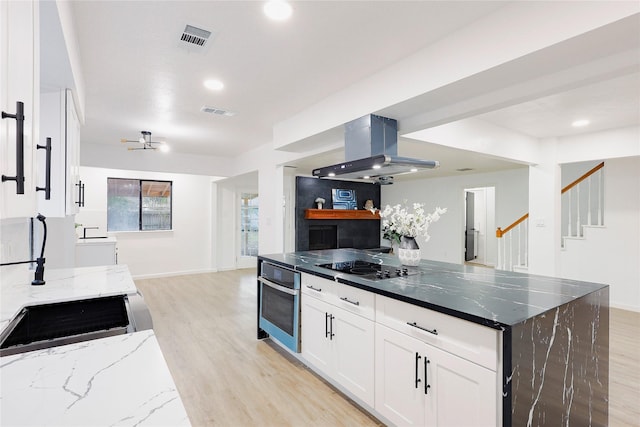 kitchen with light wood-type flooring, dark stone counters, white cabinets, oven, and range hood