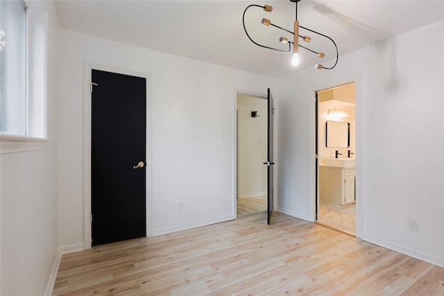 unfurnished bedroom featuring connected bathroom, sink, light hardwood / wood-style floors, and a notable chandelier