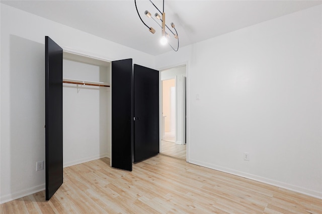 unfurnished bedroom featuring an inviting chandelier, light hardwood / wood-style flooring, and a closet