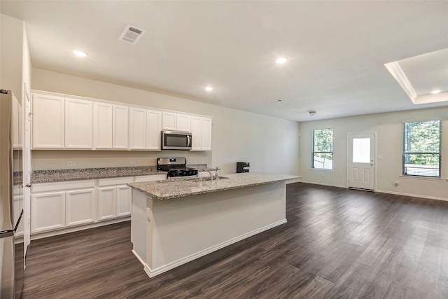 kitchen with white cabinets, dark hardwood / wood-style flooring, stainless steel appliances, light stone countertops, and a center island with sink