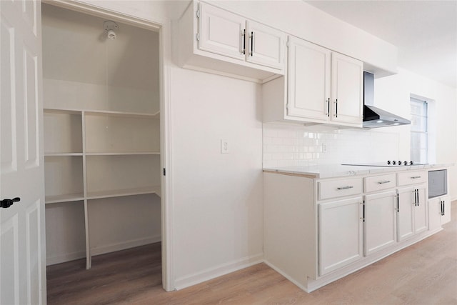 kitchen with decorative backsplash, light hardwood / wood-style floors, white cabinetry, and wall chimney range hood