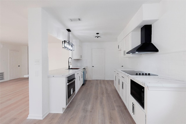 kitchen with stainless steel appliances, sink, wall chimney range hood, white cabinets, and hanging light fixtures