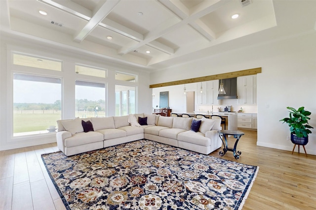 living room featuring beamed ceiling, a high ceiling, light hardwood / wood-style floors, and coffered ceiling