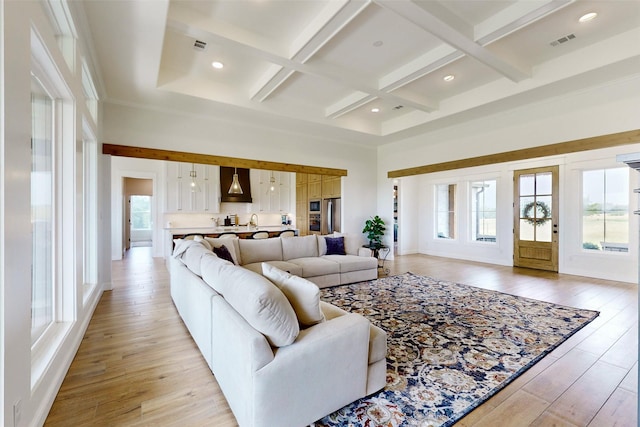 living room featuring beam ceiling, light hardwood / wood-style floors, coffered ceiling, and a high ceiling