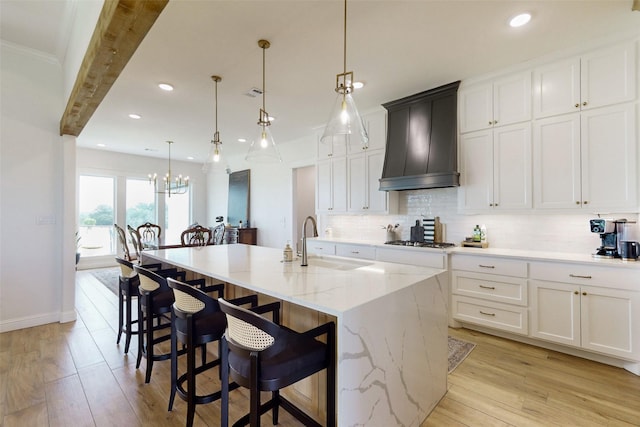 kitchen featuring sink, an island with sink, pendant lighting, and custom exhaust hood