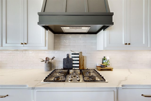 kitchen featuring light stone countertops, backsplash, stainless steel gas cooktop, exhaust hood, and white cabinetry