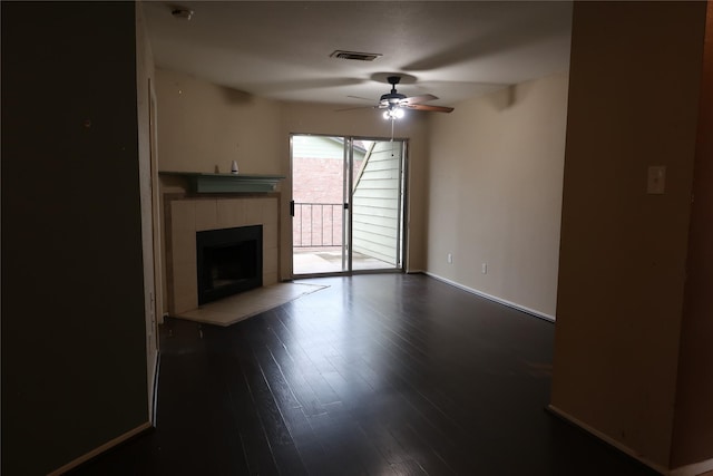 unfurnished living room featuring dark wood-type flooring, ceiling fan, and a tiled fireplace