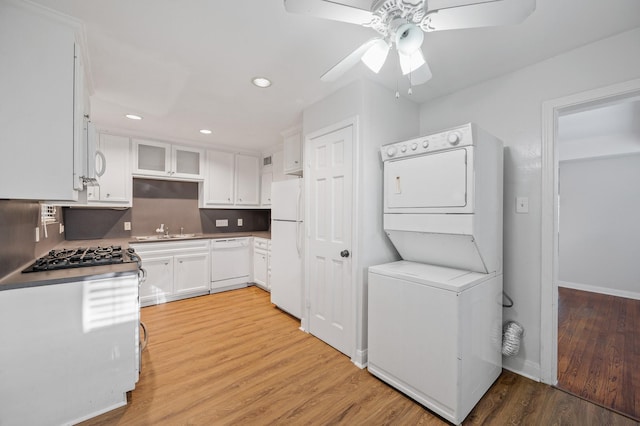 kitchen featuring sink, stacked washing maching and dryer, light hardwood / wood-style floors, white appliances, and white cabinets