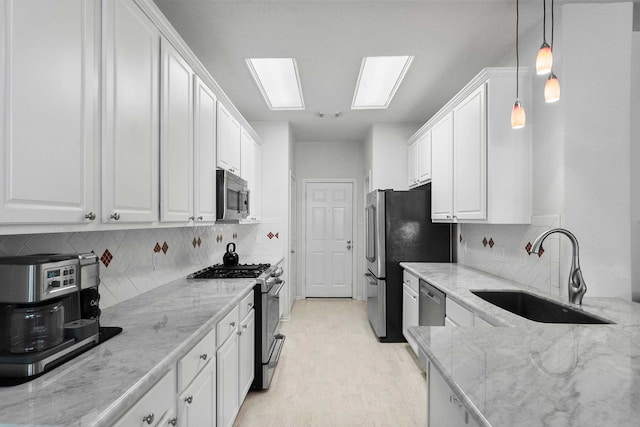 kitchen with white cabinets, sink, light stone countertops, appliances with stainless steel finishes, and decorative light fixtures