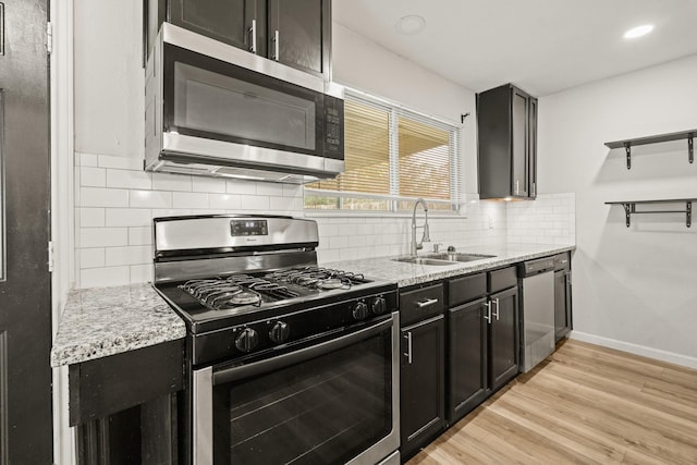 kitchen featuring light stone countertops, light wood-type flooring, stainless steel appliances, and sink