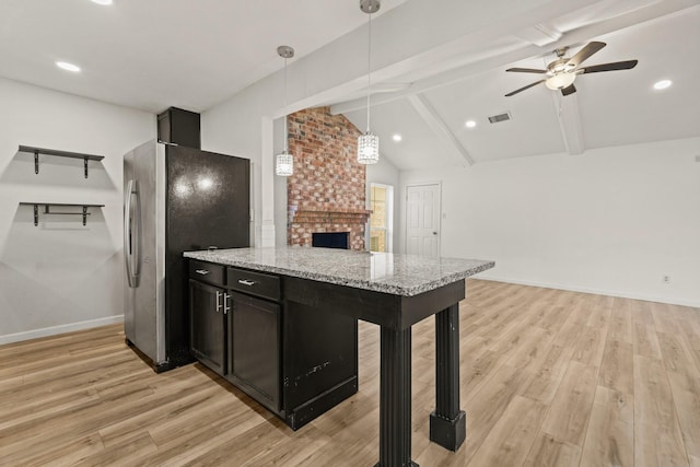 kitchen with light stone countertops, stainless steel fridge, a brick fireplace, ceiling fan, and pendant lighting