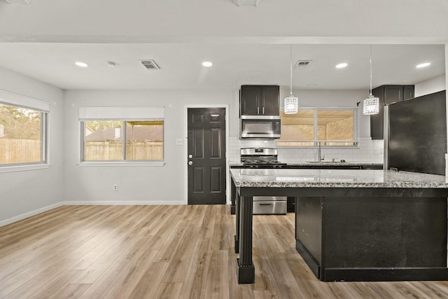 kitchen with appliances with stainless steel finishes, light stone counters, a wealth of natural light, sink, and hanging light fixtures