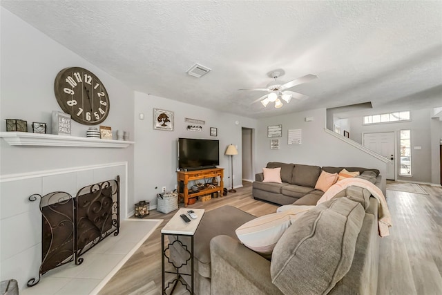 living room with a textured ceiling, light wood-type flooring, and ceiling fan