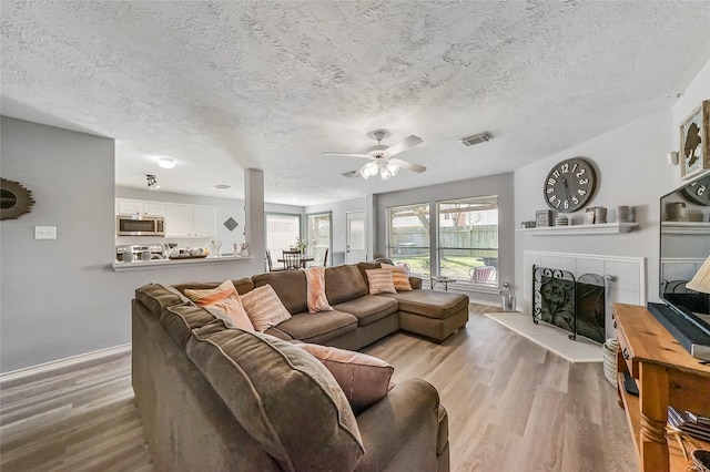 living room with a tile fireplace, a textured ceiling, light hardwood / wood-style floors, and ceiling fan