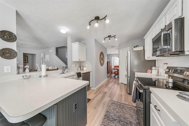 kitchen with white cabinetry, kitchen peninsula, light hardwood / wood-style floors, a breakfast bar, and appliances with stainless steel finishes