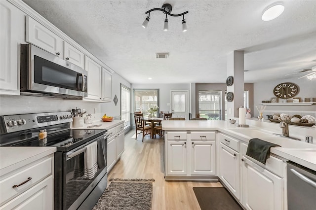 kitchen with sink, a textured ceiling, appliances with stainless steel finishes, light hardwood / wood-style floors, and white cabinetry