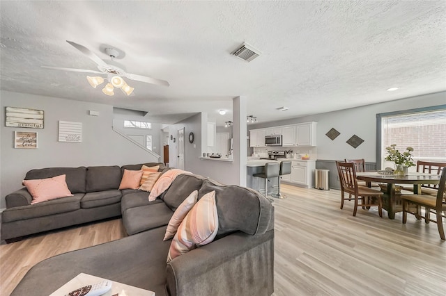 living room featuring ceiling fan, light wood-type flooring, and a textured ceiling